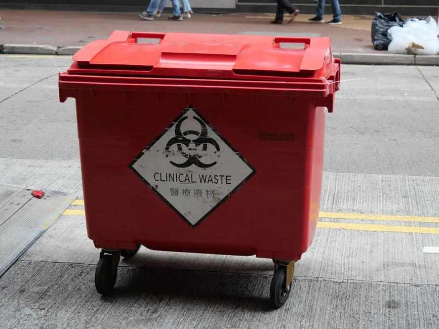 A red wheeled bin labeled for clinical waste management on a city street.