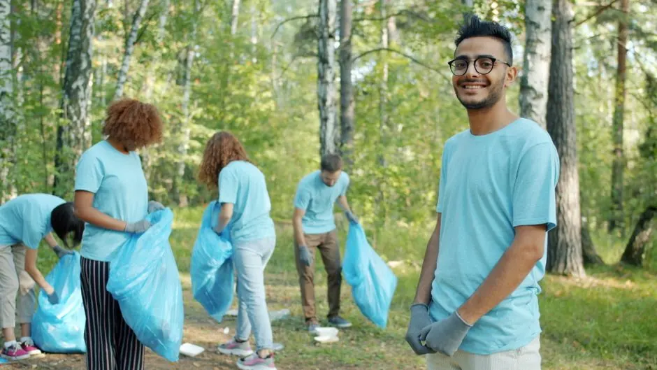 Diverse group of young volunteers cleaning up litter in a forest area on a sunny day.